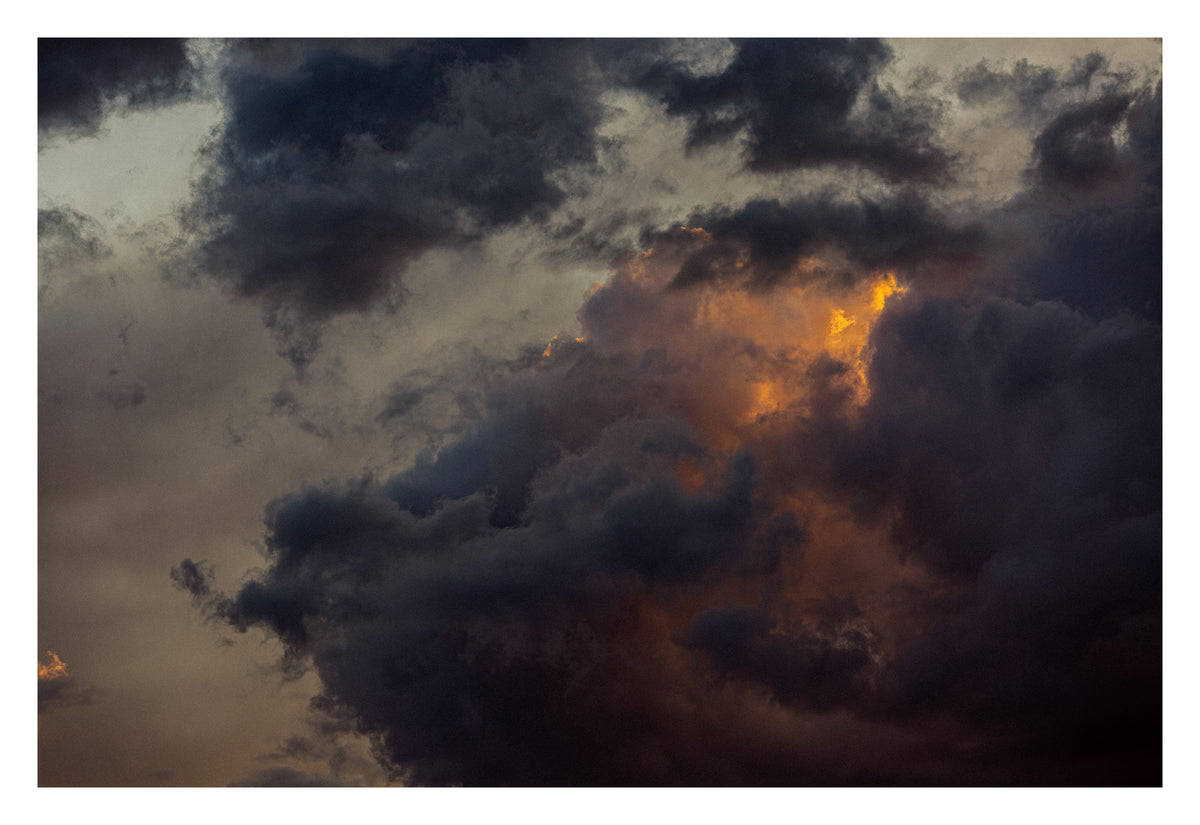 Dense storm cloud formations lit by a single beam of light. Shown with the white signing border.