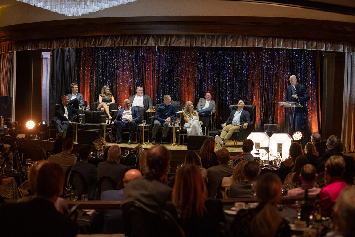 A corporate event on stage, guests seated in the dark ballroom