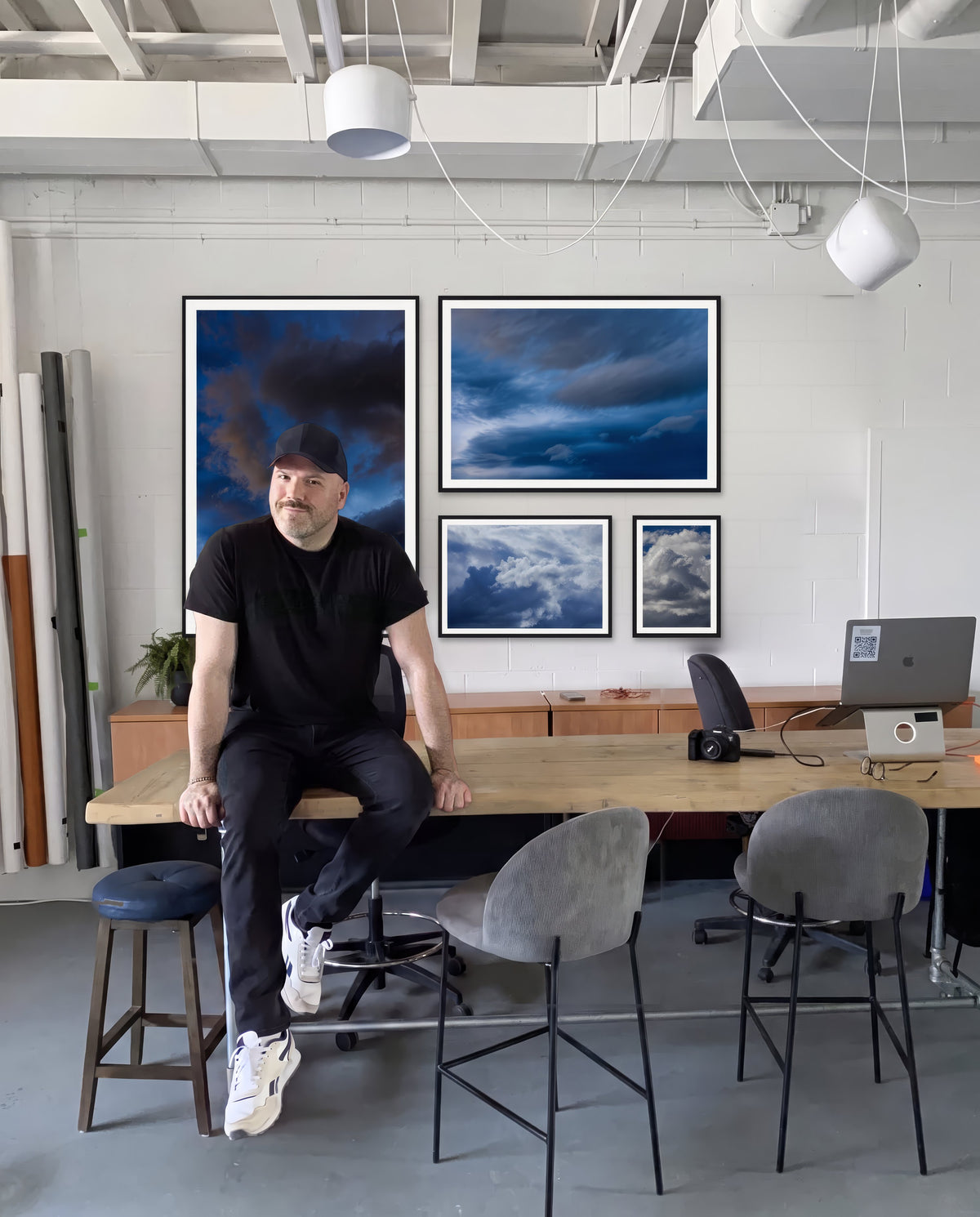 Phil Crozier sitting on a studio table in front of a wall of framed Sky Study prints.