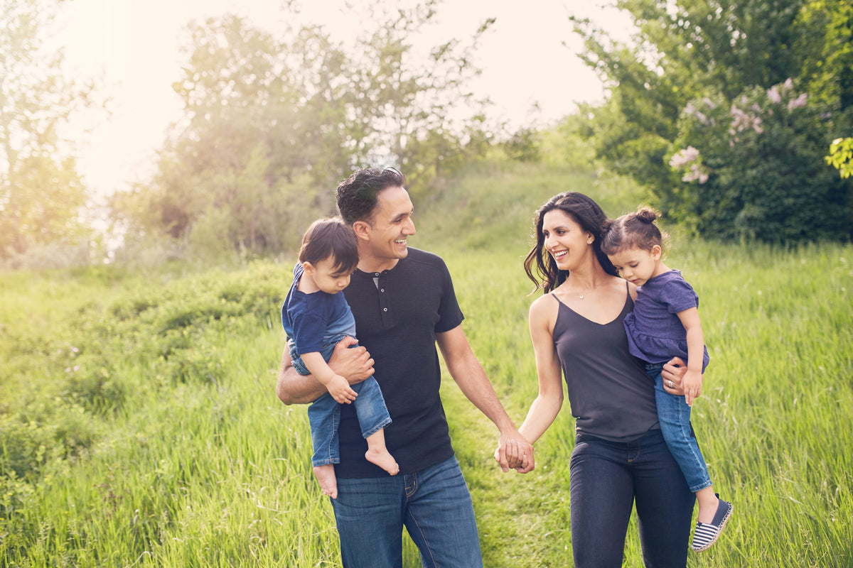 A family walking through tall summer grass, carrying their two children