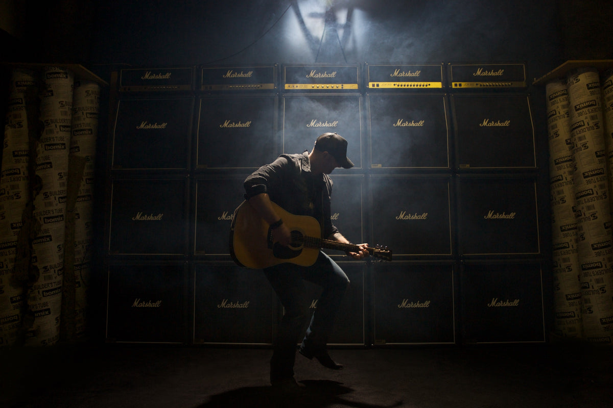 Tim Hicks with his guitar in front of a wall of Marshall amps, photographed by Phil Crozier