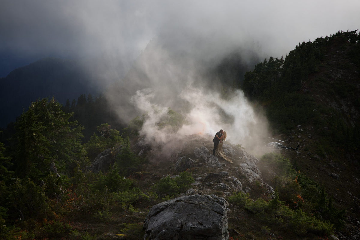 A couple on a rocky ridge as mist rises over a mountain forest